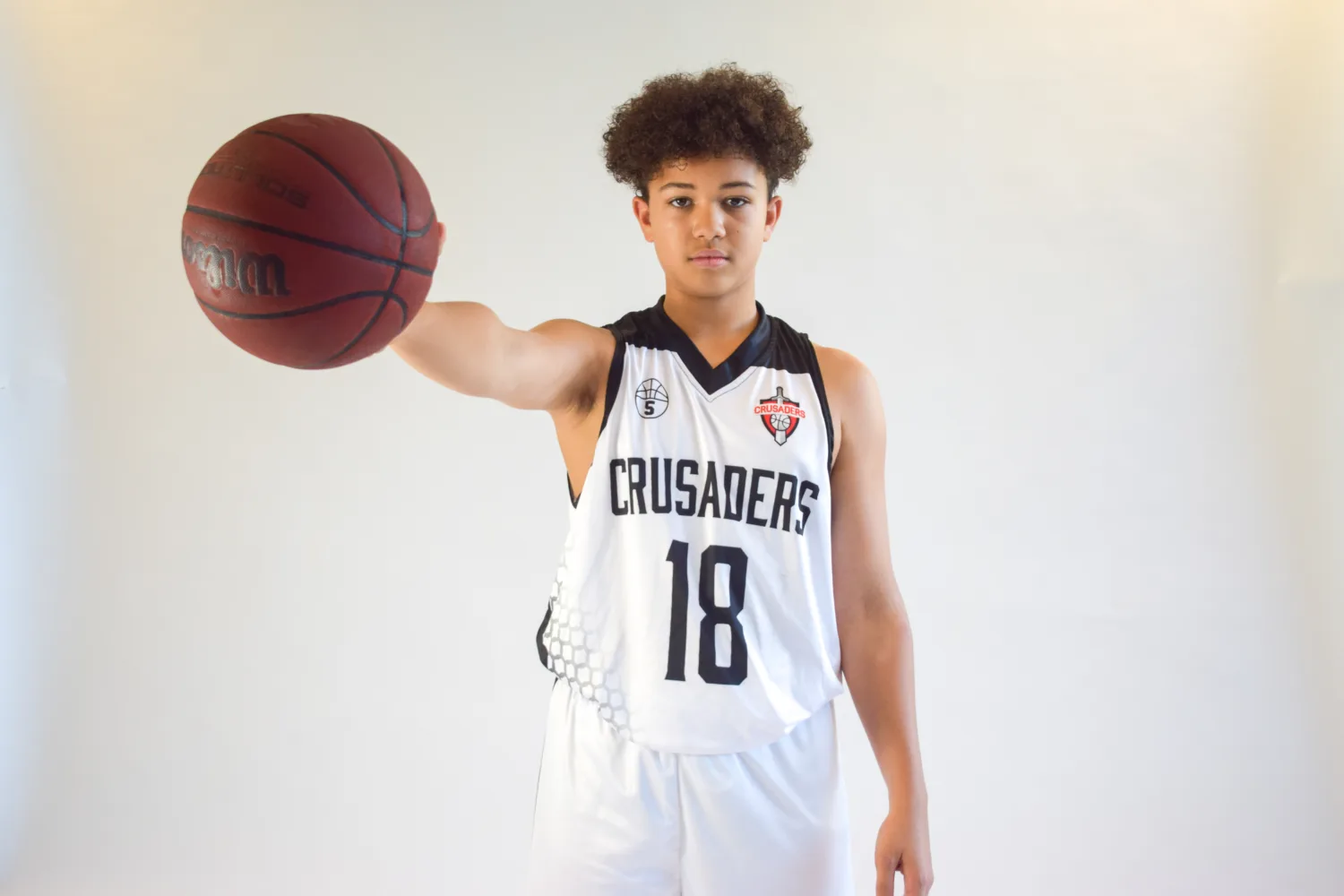 HoH student Caleb is seen dressed in a sports jersey and holding a Basketball in his right hand, looking towards the camera.