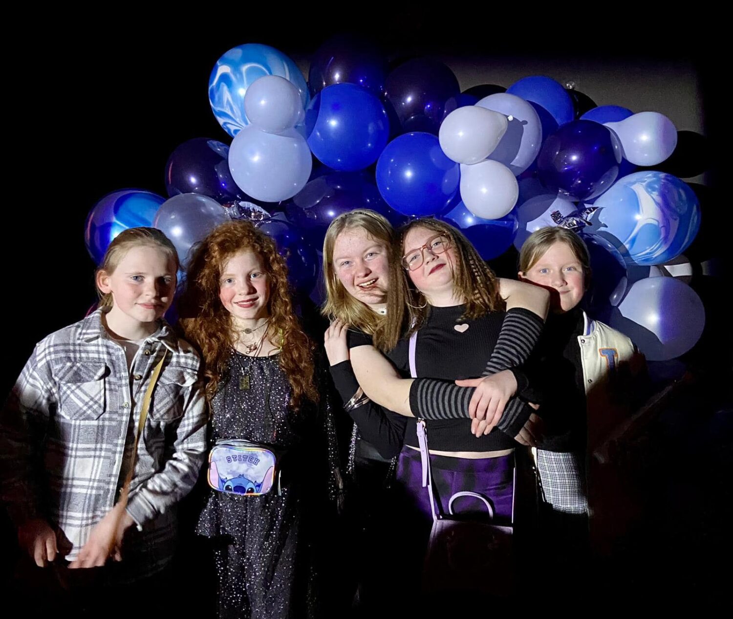 5 girls smiling for the camera with ballons behind them.